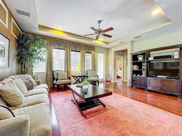 living room with ceiling fan, wood finished floors, visible vents, and a raised ceiling