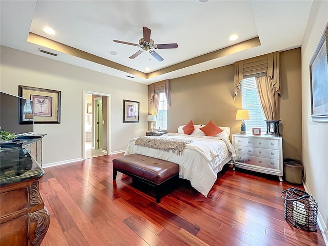 bedroom with wood-type flooring, visible vents, a raised ceiling, and multiple windows