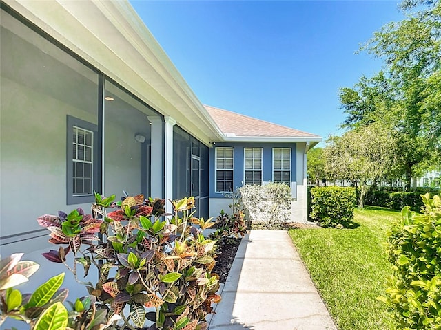 entrance to property with a yard, a shingled roof, and stucco siding