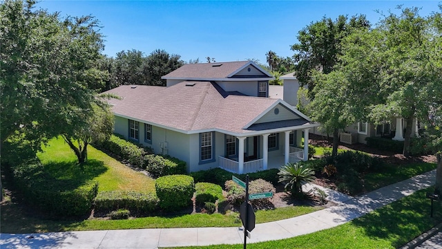 view of front of property with stucco siding, a shingled roof, a front yard, and covered porch