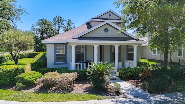 view of front facade with stucco siding, a shingled roof, and covered porch