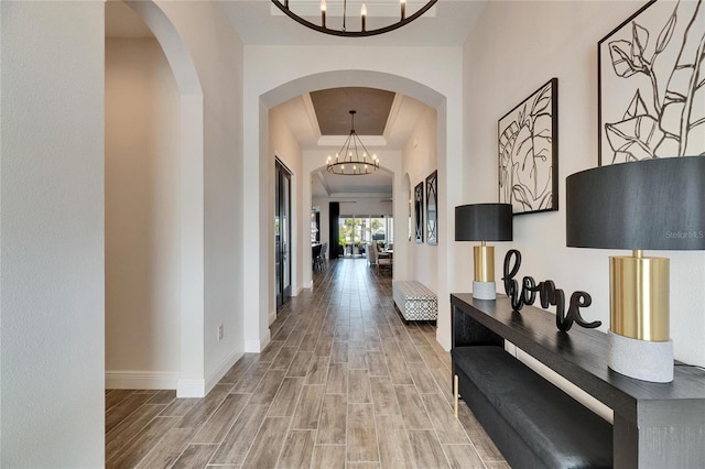hallway featuring crown molding, a tray ceiling, a chandelier, wood tiled floor, and baseboards