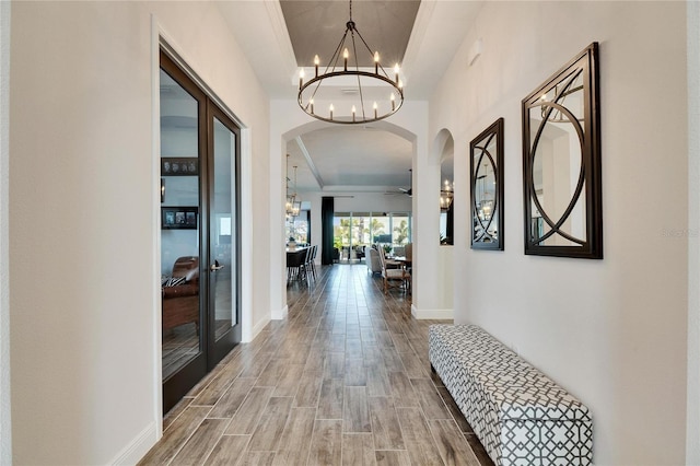 corridor featuring arched walkways, a notable chandelier, wood finished floors, and a raised ceiling