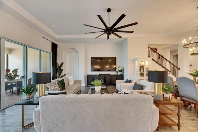 living room featuring arched walkways, ceiling fan with notable chandelier, ornamental molding, and stairway