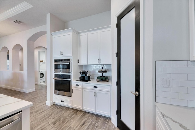 kitchen featuring visible vents, appliances with stainless steel finishes, backsplash, light wood-style flooring, and washer / dryer