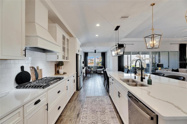 kitchen featuring tasteful backsplash, a sink, open floor plan, appliances with stainless steel finishes, and custom range hood