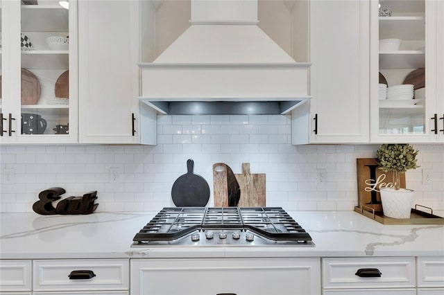 kitchen featuring stainless steel gas cooktop, custom range hood, white cabinetry, and glass insert cabinets