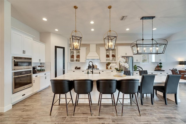 kitchen with a large island, premium range hood, visible vents, stainless steel appliances, and a sink