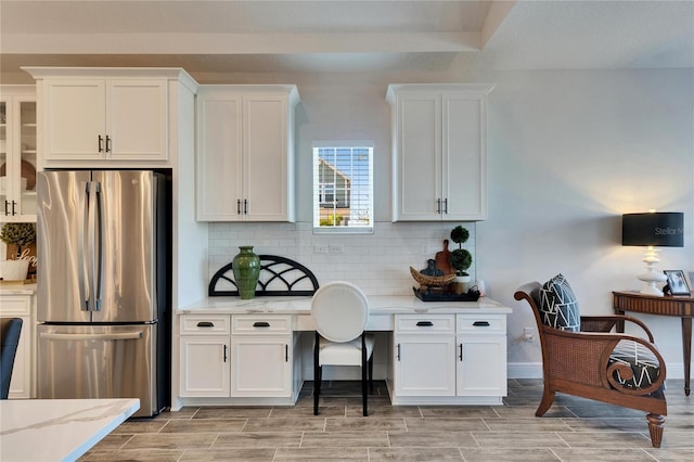 kitchen featuring freestanding refrigerator, white cabinetry, wood finish floors, backsplash, and light stone counters