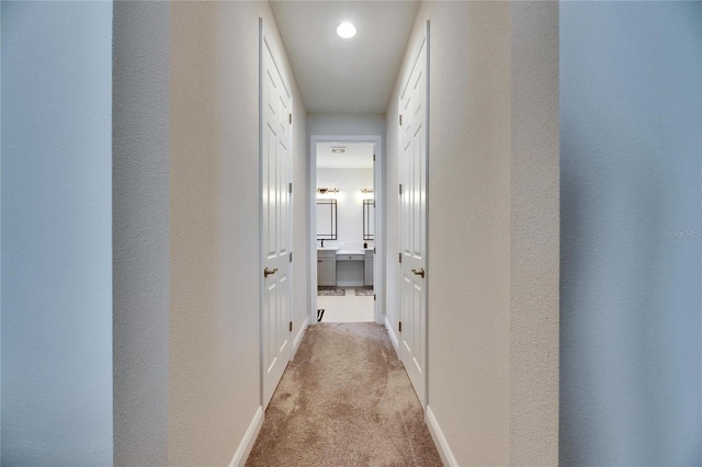 hallway with light carpet, a textured wall, and baseboards