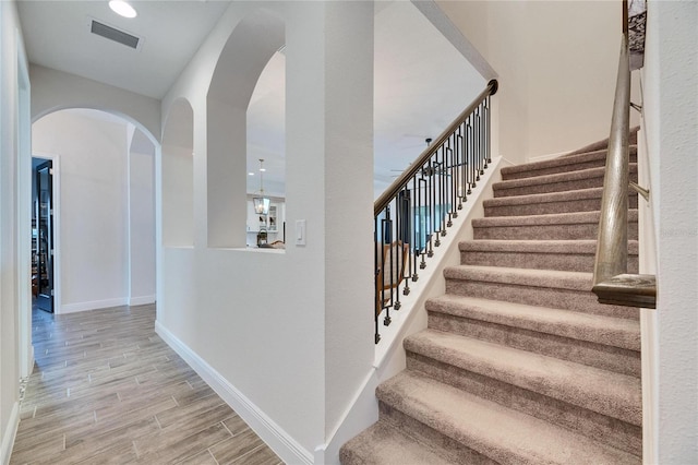 staircase with arched walkways, visible vents, baseboards, and wood finish floors