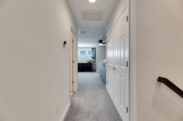 hallway with carpet flooring, visible vents, baseboards, and attic access