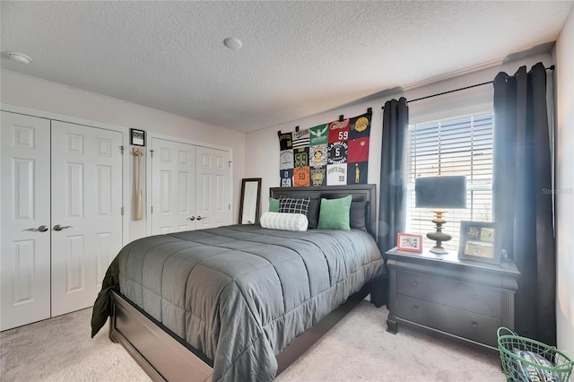 bedroom with two closets, light carpet, and a textured ceiling