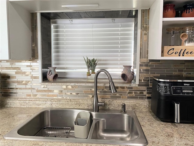 details featuring light stone counters, tasteful backsplash, and a sink