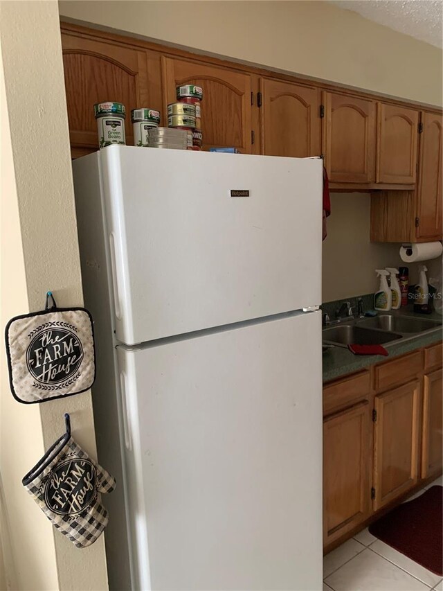 7526 Needle Leaf Pl Unit 30, Tampa, FL 33617 - kitchen with light tile patterned floors, brown cabinetry, freestanding refrigerator, and a sink