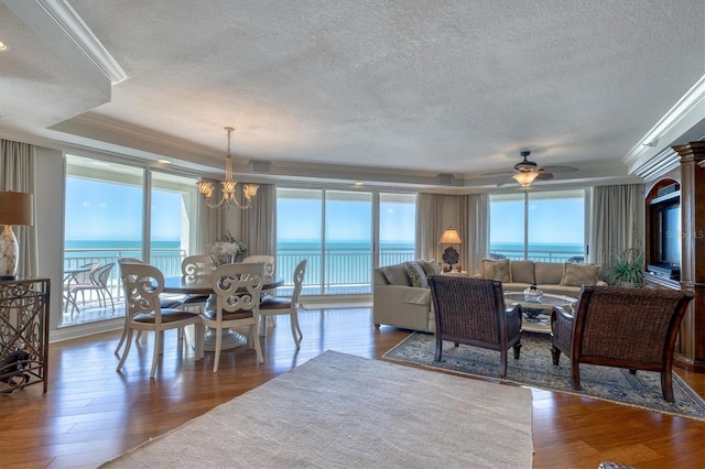 living area with wood finished floors, a textured ceiling, crown molding, and a raised ceiling