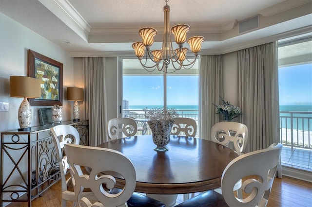 dining area with a raised ceiling, a notable chandelier, a water view, crown molding, and hardwood / wood-style floors