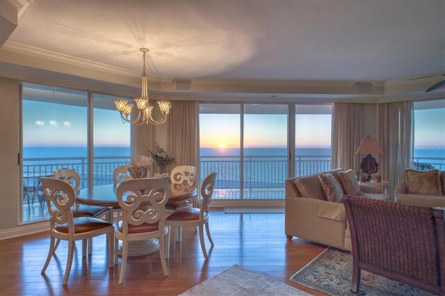 dining area with crown molding, wood finished floors, an inviting chandelier, and a water view