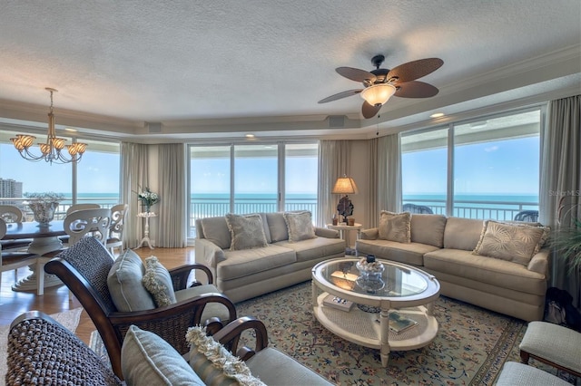 living area with a water view, light wood-style floors, a textured ceiling, crown molding, and ceiling fan with notable chandelier