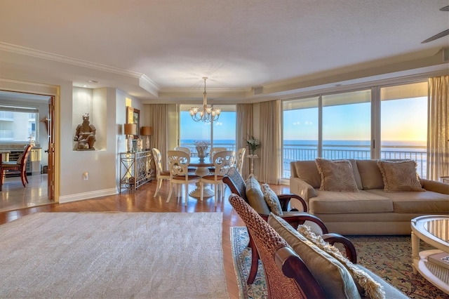 living area featuring baseboards, a notable chandelier, a water view, ornamental molding, and wood finished floors