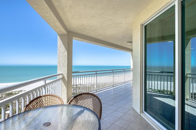 balcony featuring outdoor dining space, a beach view, and a water view