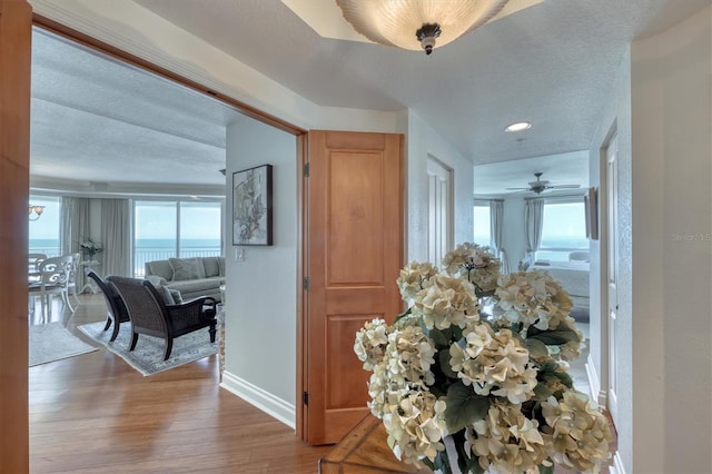 corridor featuring recessed lighting, baseboards, a textured ceiling, and wood finished floors