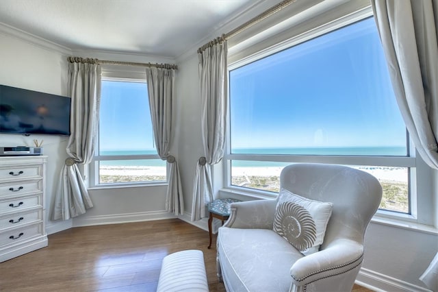 sitting room featuring a water view, baseboards, ornamental molding, and wood finished floors