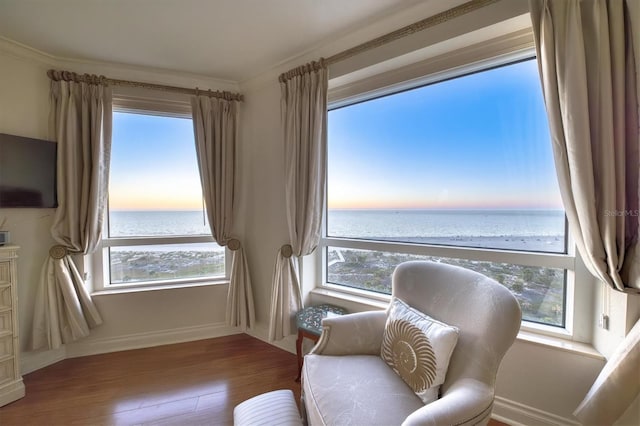 sitting room featuring a water view, baseboards, crown molding, and wood finished floors