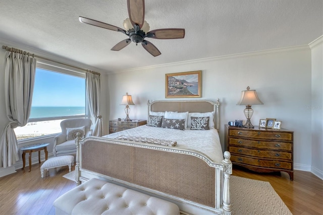 bedroom with crown molding, ceiling fan, a textured ceiling, wood finished floors, and baseboards