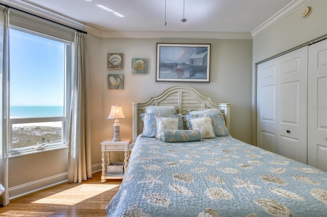 bedroom with wood finished floors, a closet, ornamental molding, and baseboards