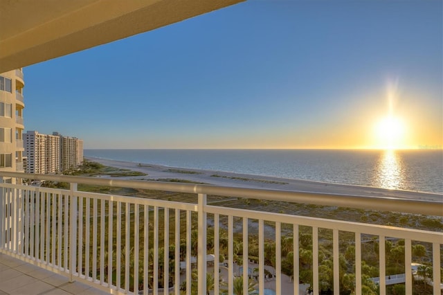 balcony at dusk featuring a water view and a view of the beach