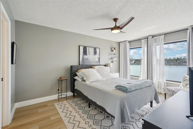 6277 Bahia Del Mar Blvd Unit 210, Saint Petersburg, FL 33715 - bedroom featuring light wood-style flooring, a textured ceiling, a water view, ceiling fan, and baseboards