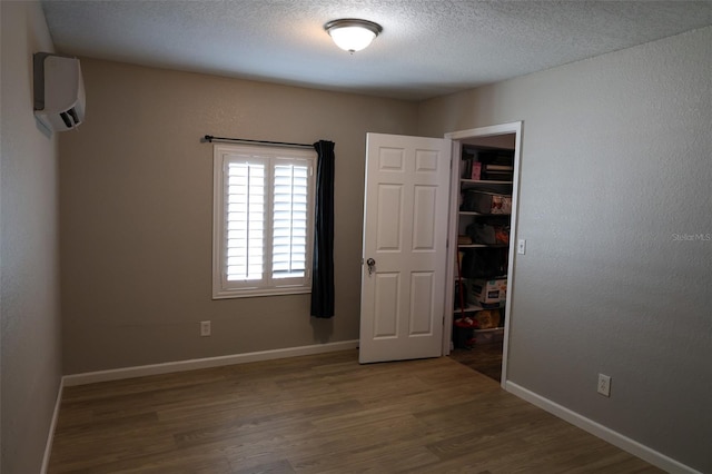 11233 51st Ave N, Saint Petersburg, FL 33708 - unfurnished bedroom with a closet, baseboards, a wall mounted air conditioner, a textured ceiling, and wood finished floors