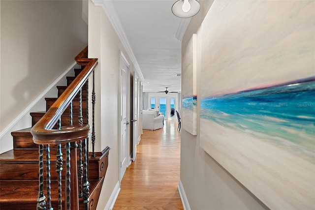 hallway with light wood-type flooring, stairway, french doors, crown molding, and baseboards