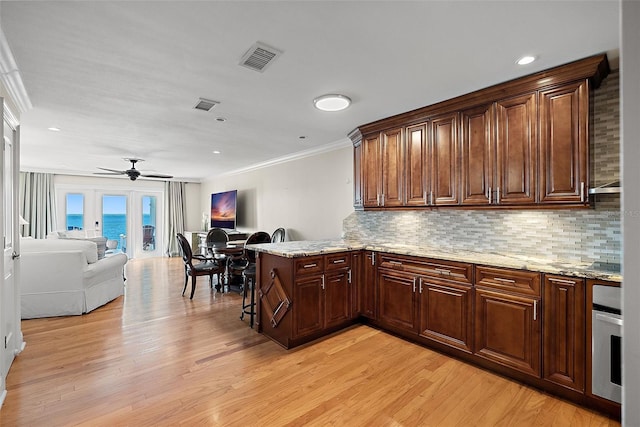 kitchen featuring visible vents, light wood-style floors, a peninsula, decorative backsplash, and ceiling fan