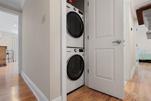 washroom featuring crown molding, stacked washer and clothes dryer, and light wood-type flooring