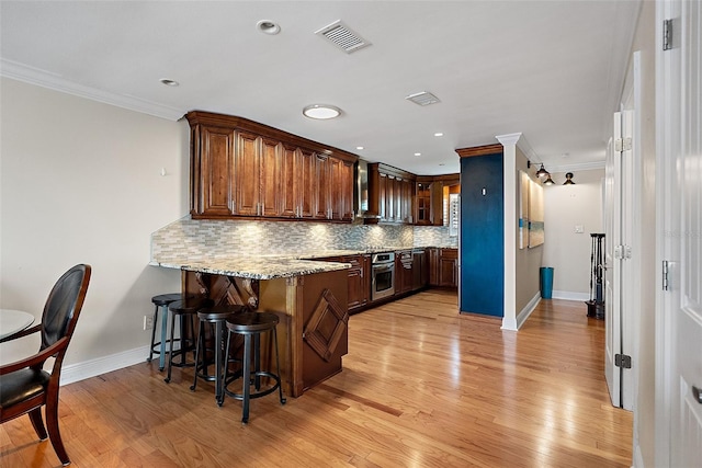 kitchen featuring backsplash, crown molding, stainless steel oven, a peninsula, and a kitchen breakfast bar