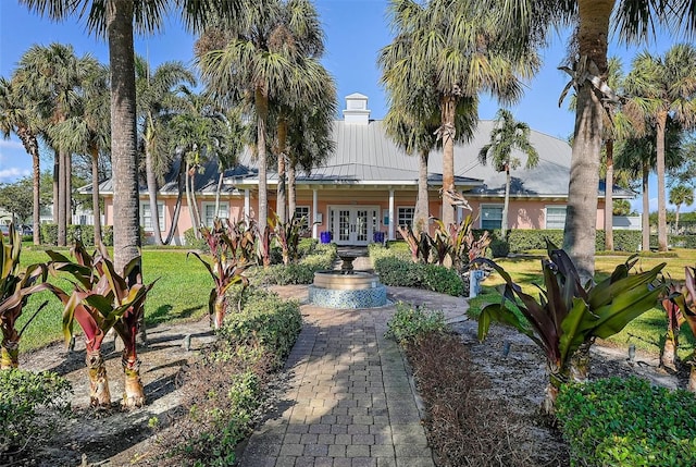 view of front facade with french doors, metal roof, a front yard, and stucco siding