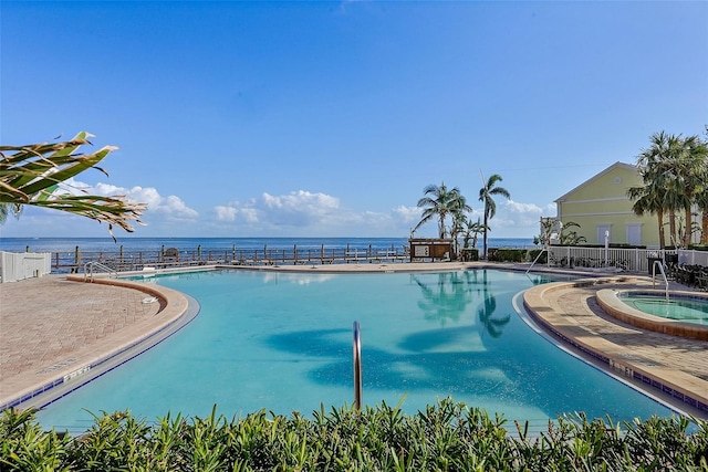 community pool with fence, a water view, and a hot tub
