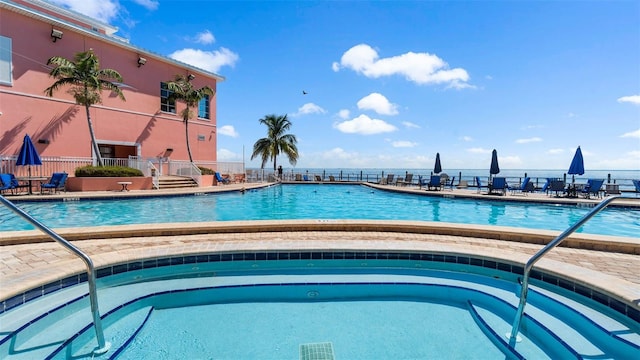 community pool with a patio area, a hot tub, and fence