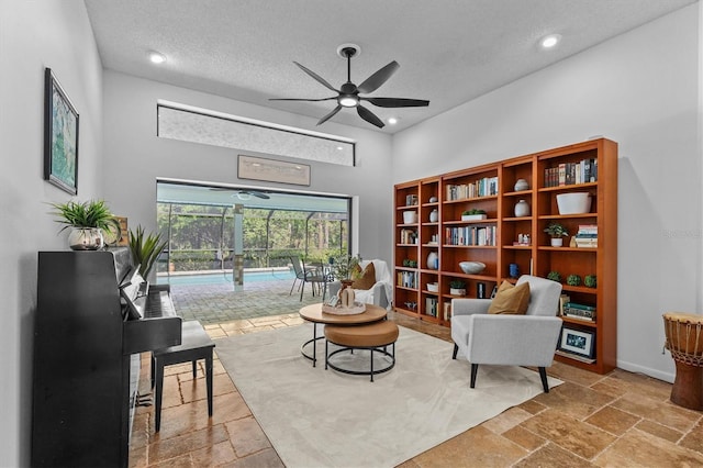 living area with baseboards, stone tile floors, a sunroom, a textured ceiling, and a ceiling fan