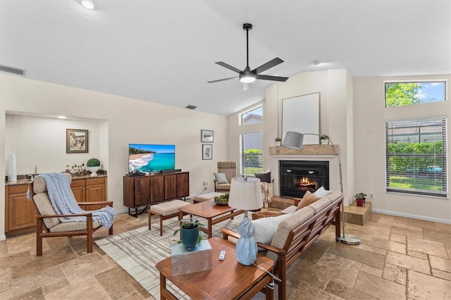 living area featuring visible vents, ceiling fan, baseboards, stone tile floors, and a glass covered fireplace