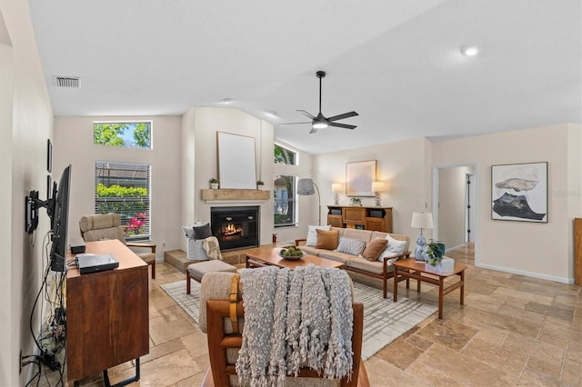 living area featuring visible vents, stone tile floors, a glass covered fireplace, baseboards, and ceiling fan