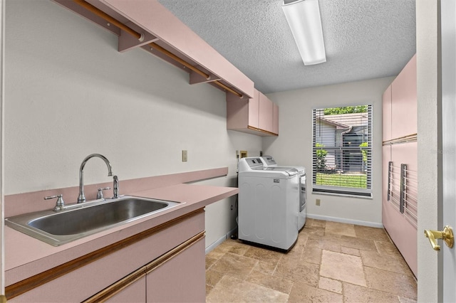 laundry room with a sink, stone tile floors, washing machine and dryer, cabinet space, and baseboards