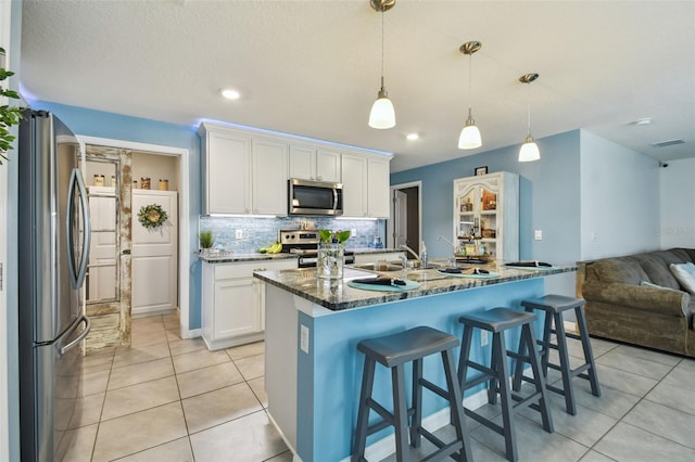 kitchen with light tile patterned flooring, stainless steel appliances, decorative backsplash, white cabinetry, and open floor plan