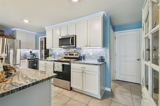 kitchen with wine cooler, appliances with stainless steel finishes, light tile patterned flooring, and white cabinetry
