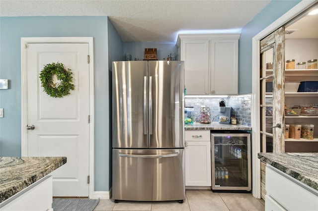 kitchen featuring backsplash, beverage cooler, freestanding refrigerator, light tile patterned flooring, and white cabinets