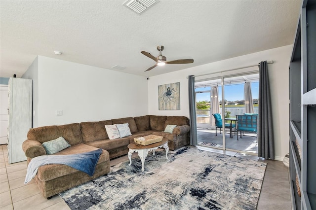 living room featuring light tile patterned floors, visible vents, a textured ceiling, and a ceiling fan
