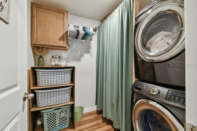 laundry area featuring baseboards, light wood finished floors, laundry area, and stacked washer / dryer