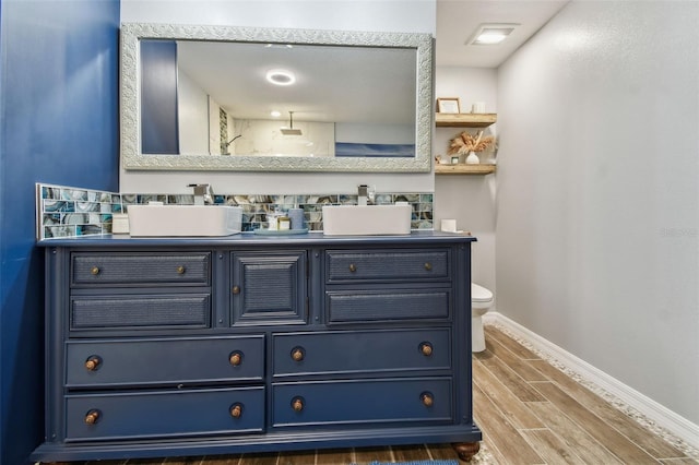bathroom featuring wood finish floors, baseboards, double vanity, and a sink
